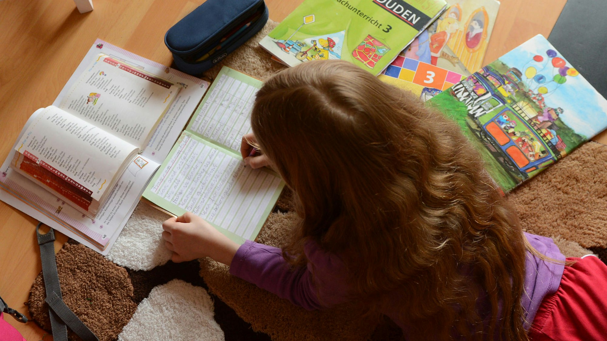 Ein Kind auf dem Boden, um es herum liegen verschiedene Schulbücher.