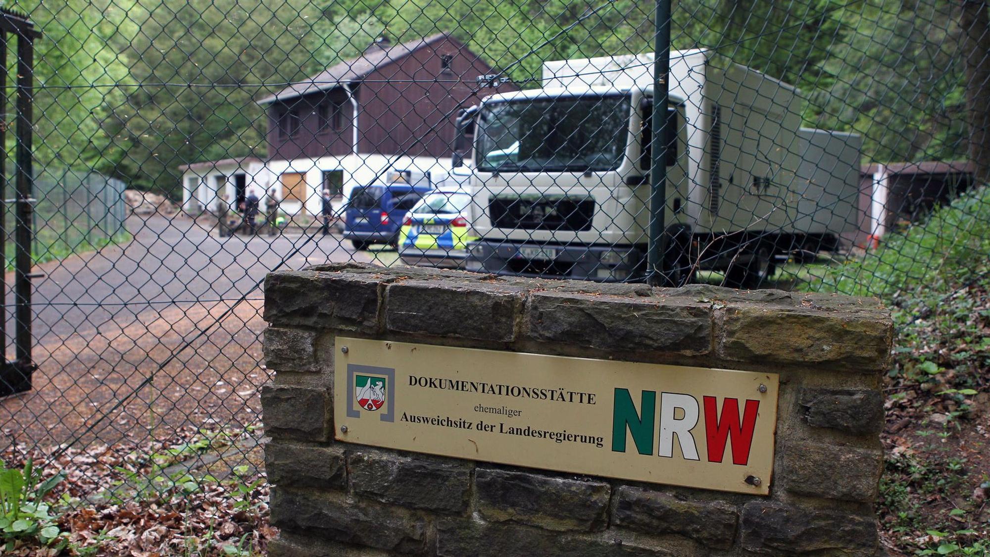 Hinter Maschendraht sieht man ein Haus, einen LKW und einen Polizeiwagen. Die Umgebung ist waldig. Über dem früheren Ausweichsitz steht ein Haus für den Bunkerwart.