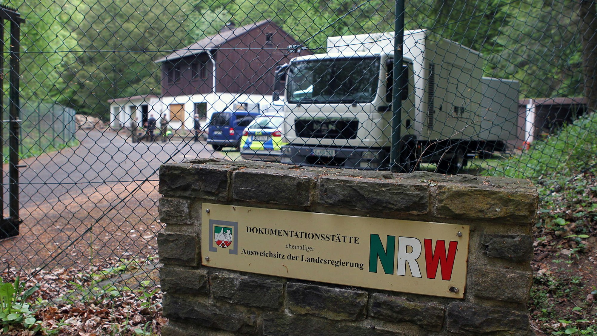 Hinter Maschendraht sieht man ein Haus, einen LKW und einen Polizeiwagen. Die Umgebung ist waldig. Über dem früheren Ausweichsitz steht ein Haus für den Bunkerwart.