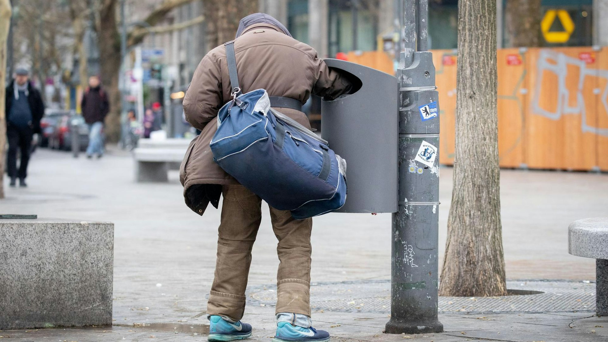 Ein Flaschensammler kontrolliert einen Mülleimer.