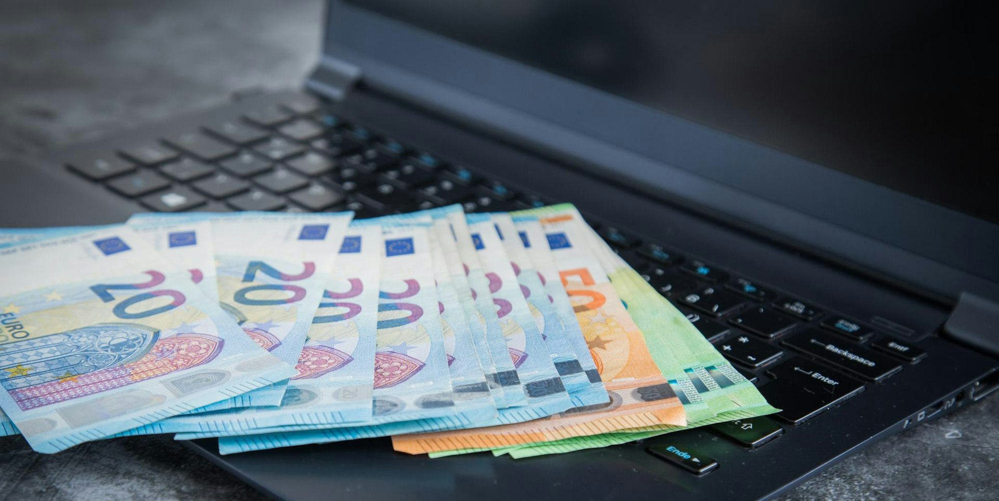 Verschiedene Euro-Scheine liegen auf einem Laptop.