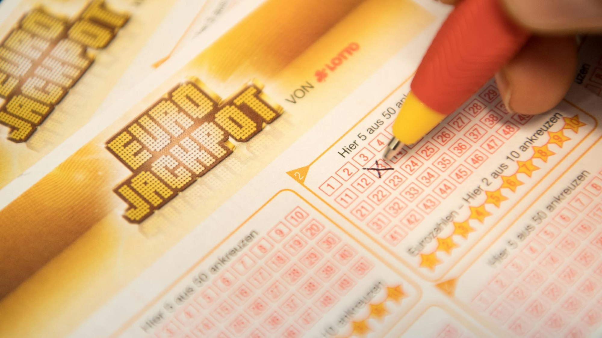 Jemand schreibt mit einem Kugelschreiber ein Kreuz auf einen Eurojackpot-Schein.