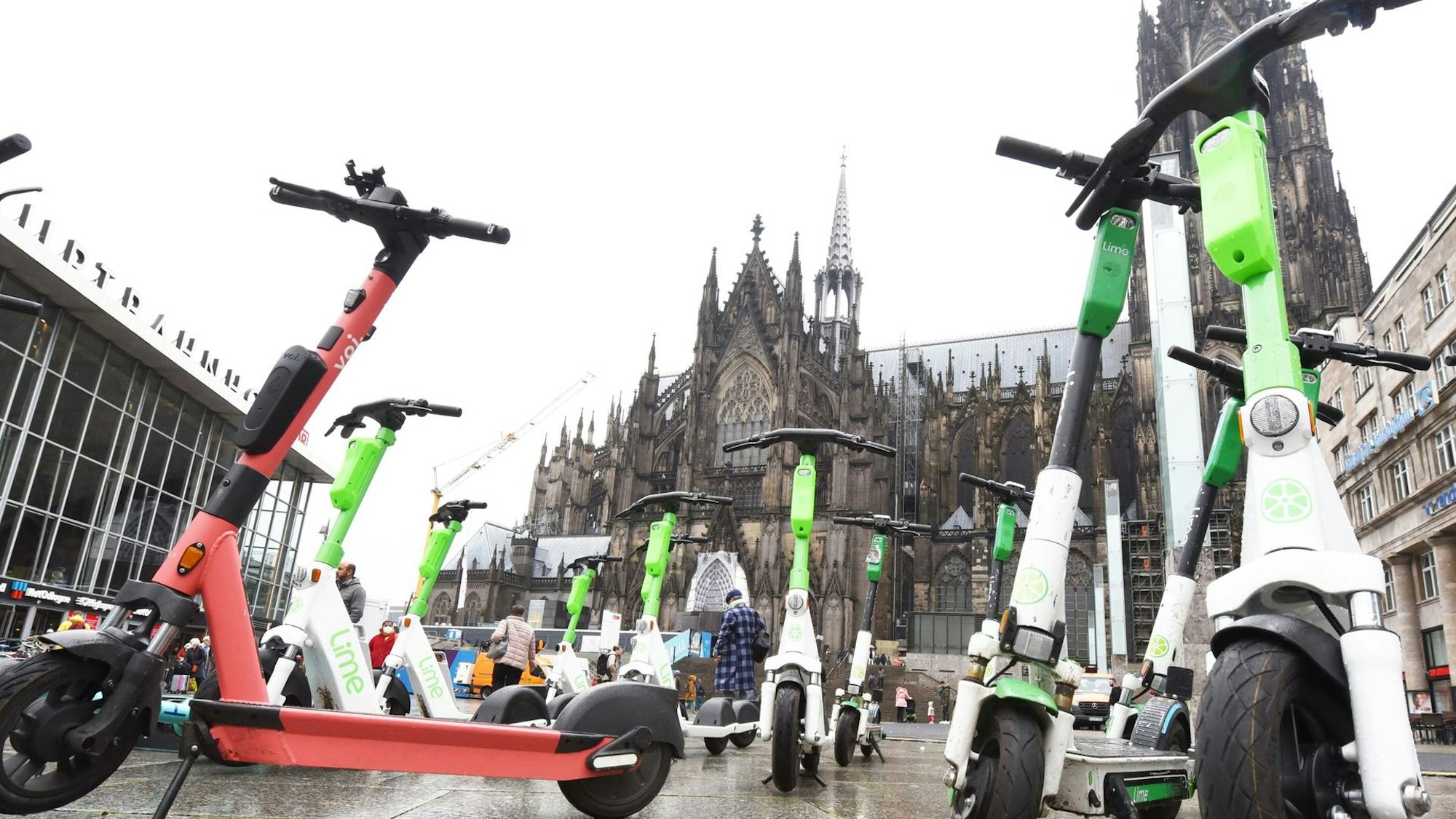 Mehrere E-Scooter sind auf dem Bahnhofsvorplatz abgestellt, im Hintergrund ist der Kölner Dom zu sehen