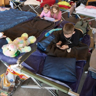 Kinder liegen mit ihren Stofftieren auf einem Matratzenlager in einer Flüchtlingtsunterkunft.