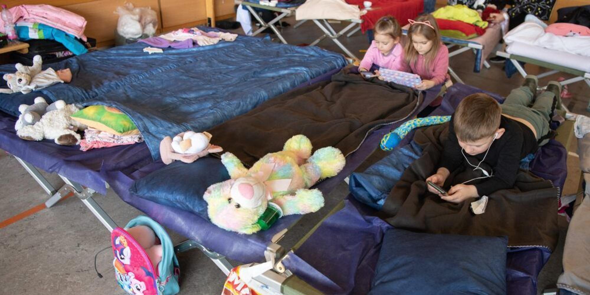Kinder liegen mit ihren Stofftieren auf einem Matratzenlager in einer Flüchtlingtsunterkunft.