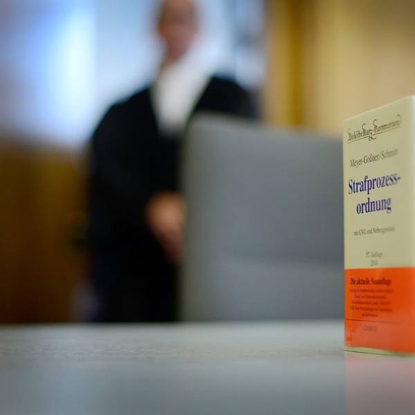 Das Foto zeigt ein Buch mit der Strafprozessordnung als Symbolbild für eine Gerichtsverhandlung, im Hintergrund einen Juristen in einer Robe.