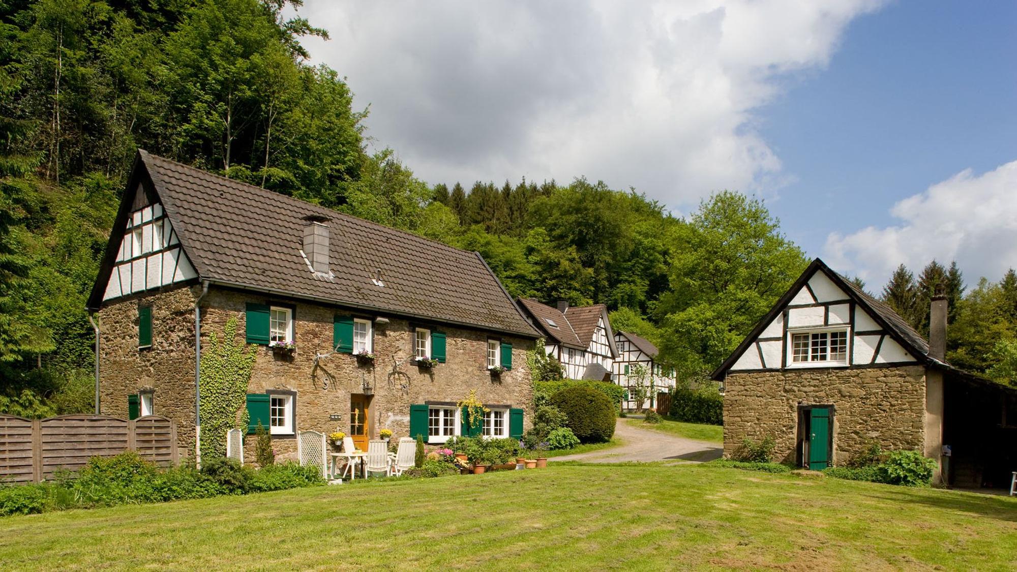 Alte Gebäude aus Stein und Fachwerk, grüne Wiese im Vordergrund.