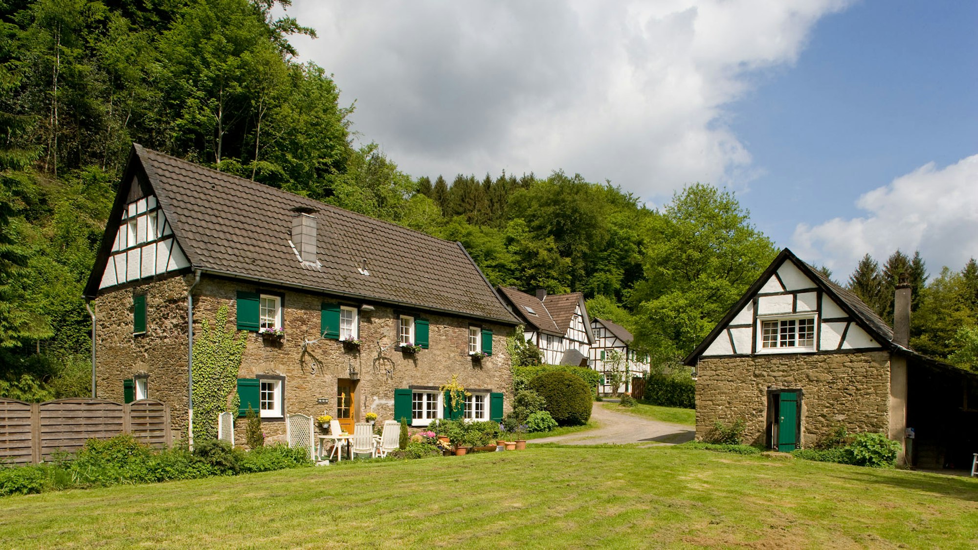 Alte Gebäude aus Stein und Fachwerk, grüne Wiese im Vordergrund.